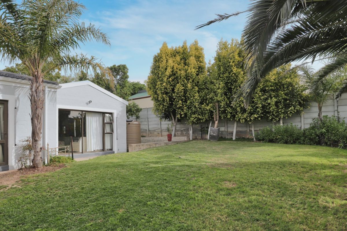 A spacious rear garden featuring a well-maintained lawn, mature palm trees, and a secure precast concrete boundary wall with direct access to the home.