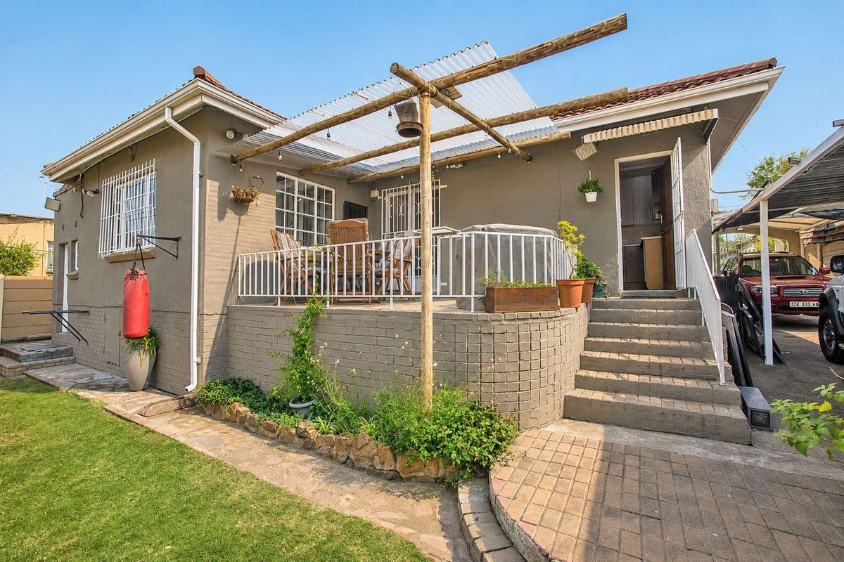 Rear exterior view featuring a raised patio with a timber pergola, brick retaining wall, and concrete stairs leading to the home entrance.