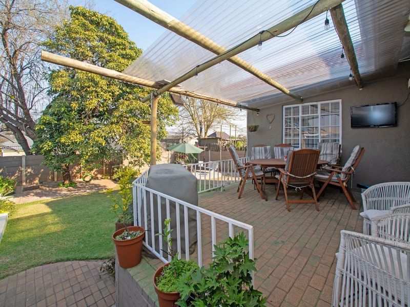Covered outdoor patio area featuring brick paving, a translucent roof structure, and a metal balustrade overlooking the garden.