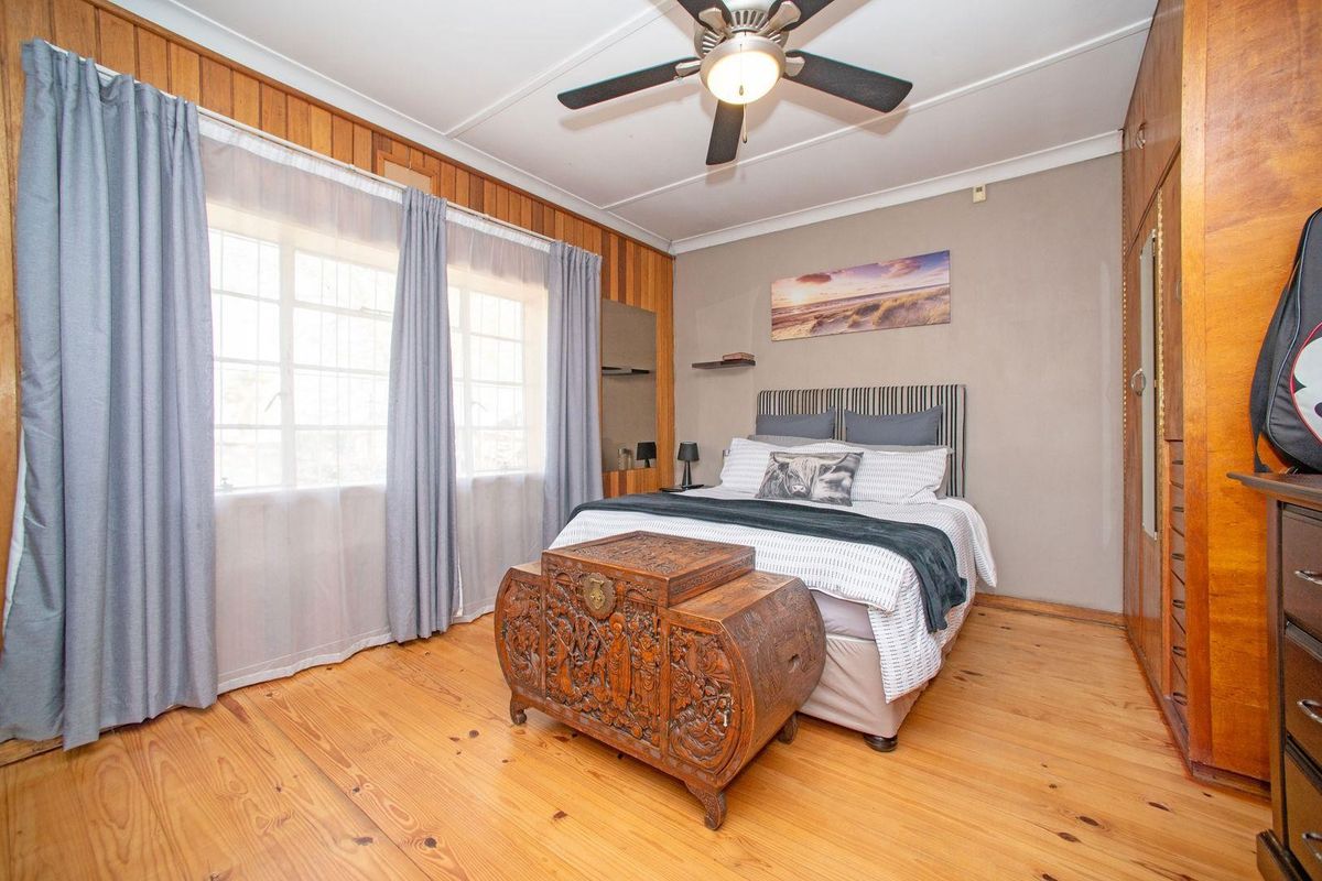 A bedroom featuring timber wall paneling, built-in cupboards, a ceiling fan, and timber flooring, offering a classic, lived-in aesthetic.