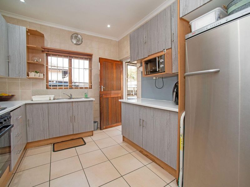 Functional kitchen featuring grey wood-grain cabinetry, tiled flooring, built-in oven and hob, and direct access to the exterior.