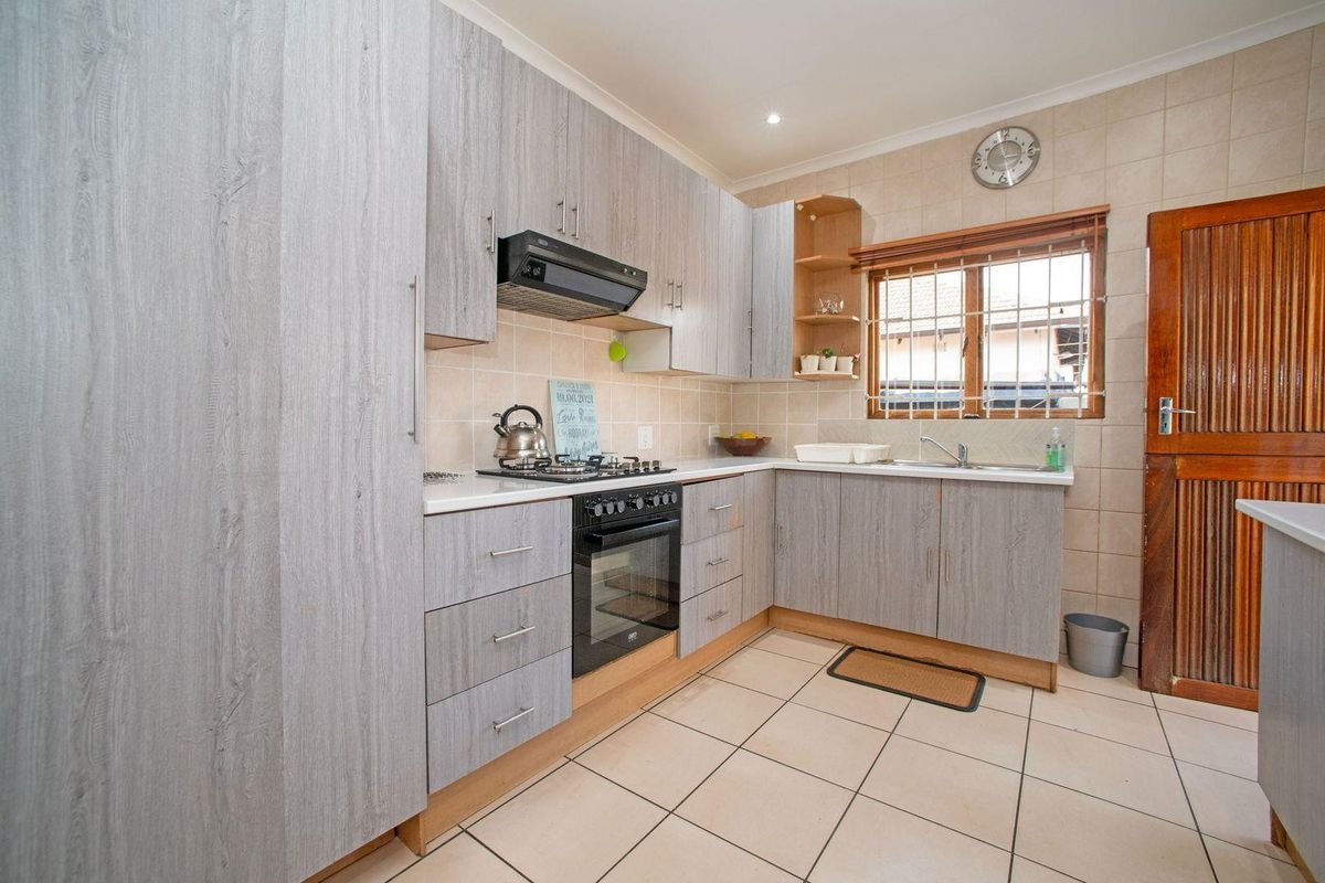 A functional kitchen featuring light wood-grain cabinetry, a gas hob with extractor, tiled flooring, and a tiled backsplash with a window view.