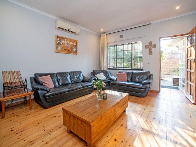 A comfortable living room featuring polished timber flooring, a wall-mounted air conditioning unit, and direct access to an outdoor patio area.