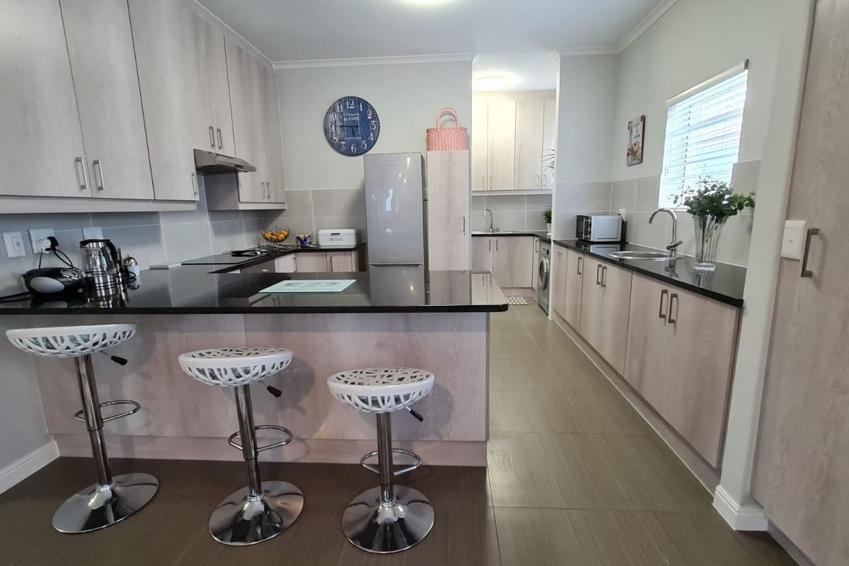 Modern kitchen featuring light wood-finish cabinetry, contrasting black granite countertops, a breakfast bar, and integrated appliances with tiled flooring throughout.