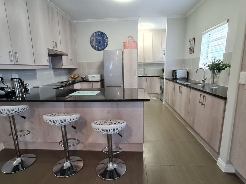 Modern kitchen featuring light wood-finish cabinetry, contrasting black granite countertops, a breakfast bar, and integrated appliances with tiled flooring throughout.