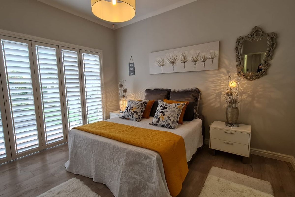 A well-maintained bedroom featuring light-toned laminate flooring and white plantation shutters that provide natural light control.