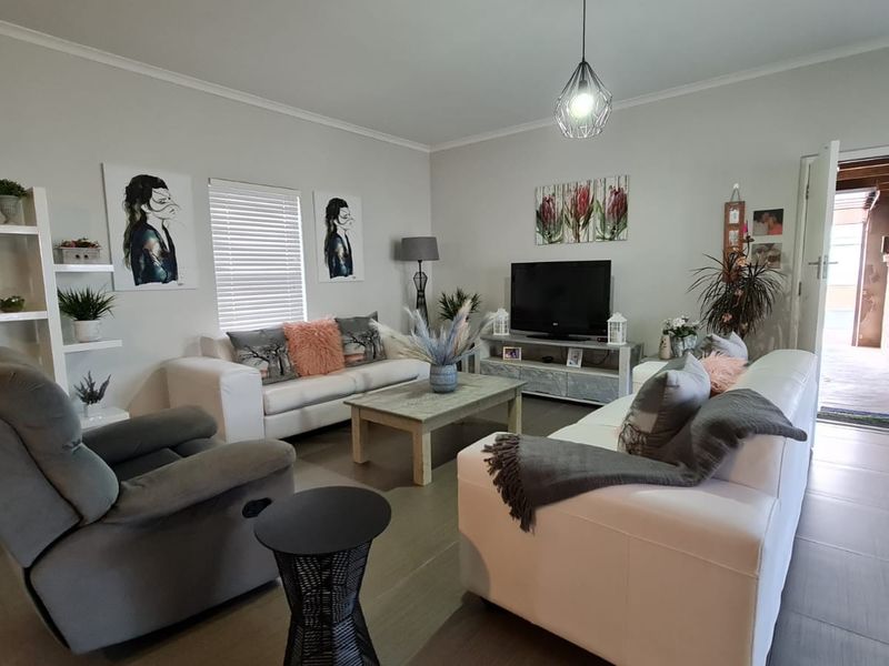A well-maintained living room featuring neutral tiled flooring, venetian blinds, and a modern pendant light fixture.