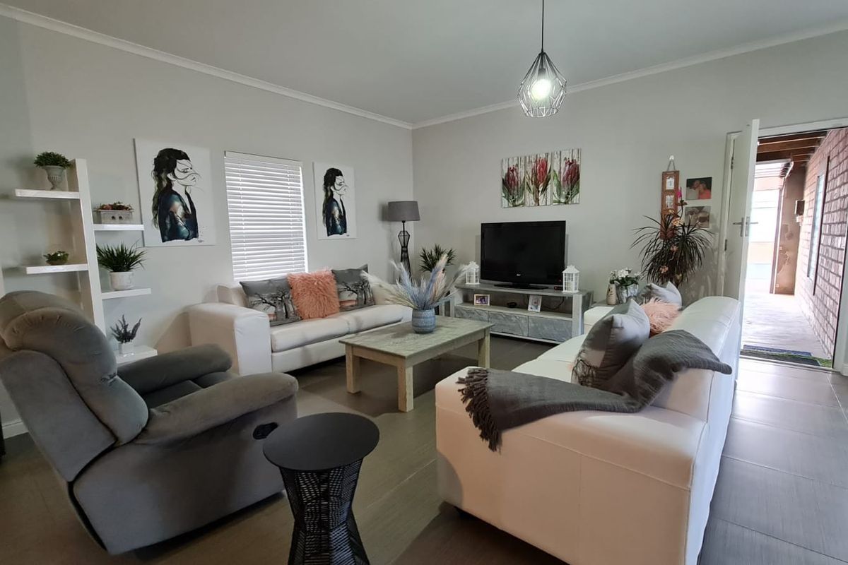 A well-maintained living room featuring neutral tiled flooring, venetian blinds, and a modern pendant light fixture.