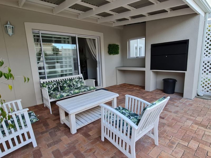 A covered patio area featuring brick paving, a built-in braai, and direct access to the interior through a sliding door.