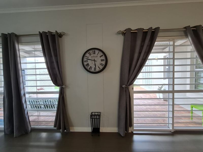 A bright living area featuring dual sliding glass doors with security gates, neutral walls, and modern laminate flooring, offering a view of the outdoor patio.