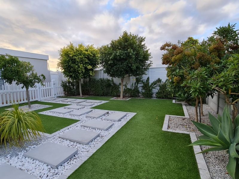 A well-maintained landscaped garden featuring artificial turf, concrete stepping stones, white gravel borders, and secure perimeter fencing.