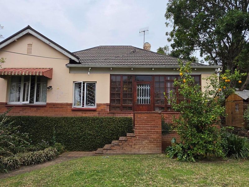 Front elevation of a traditional house featuring a tiled roof, brick base, and timber-framed windows with security gates.