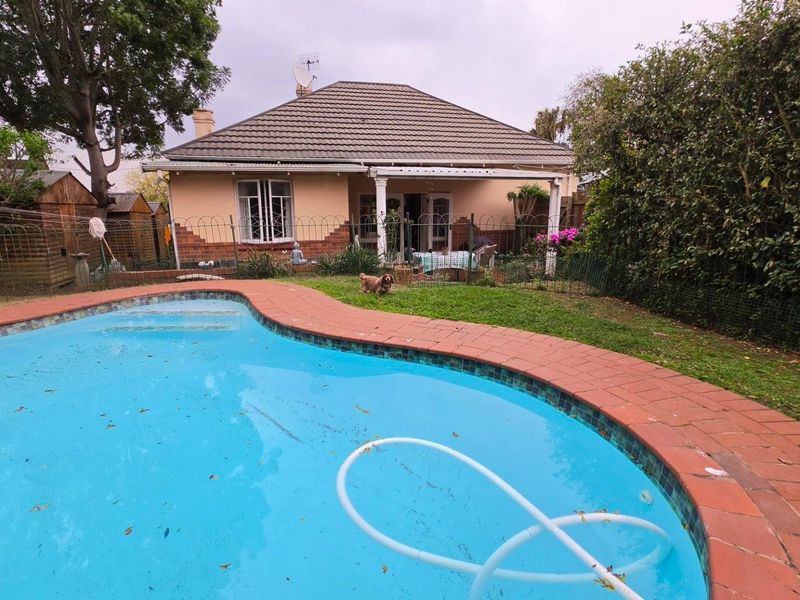 Rear view of the property featuring a swimming pool with brick coping, a small lawn area, and a covered patio attached to the main house.