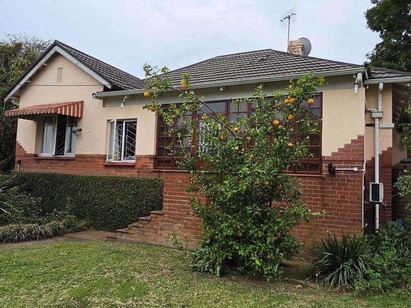 Front elevation of a traditional brick house featuring a tiled roof, timber-framed windows, and established garden surroundings.