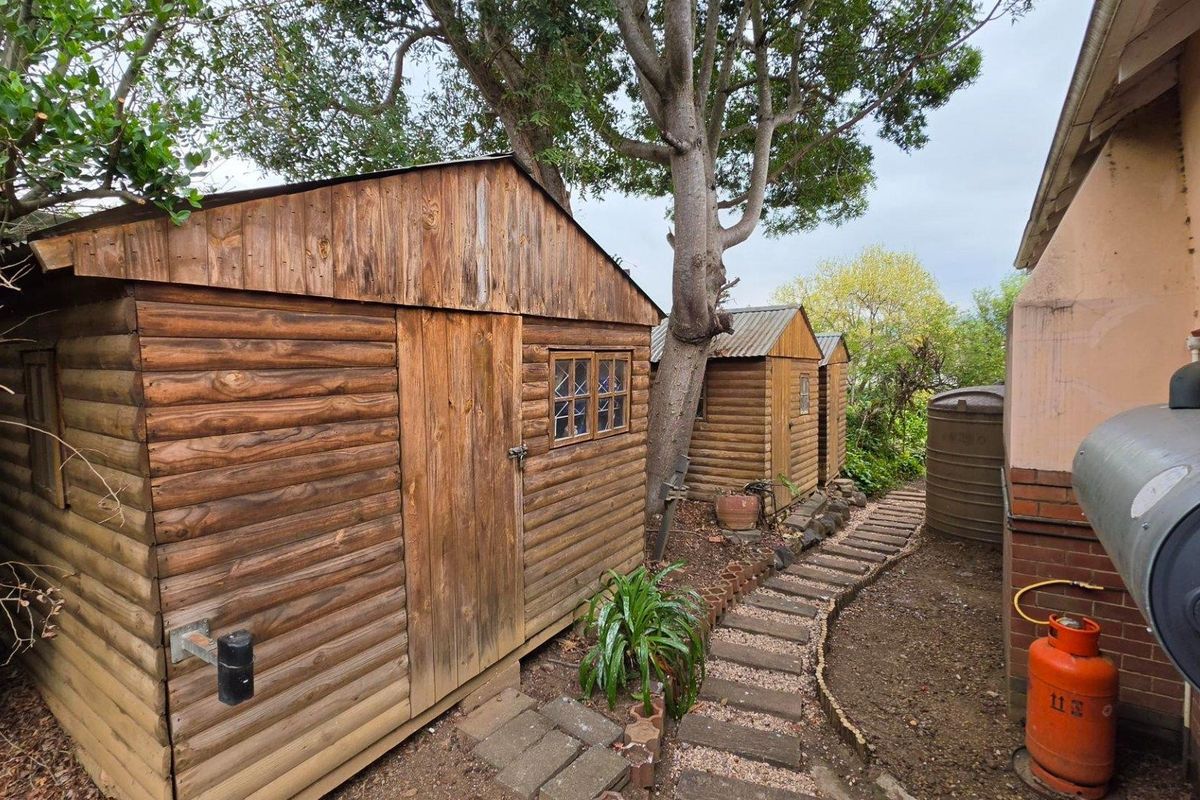 Rear garden area featuring two wooden storage sheds, a water tank, and a paved pathway alongside the main house structure.