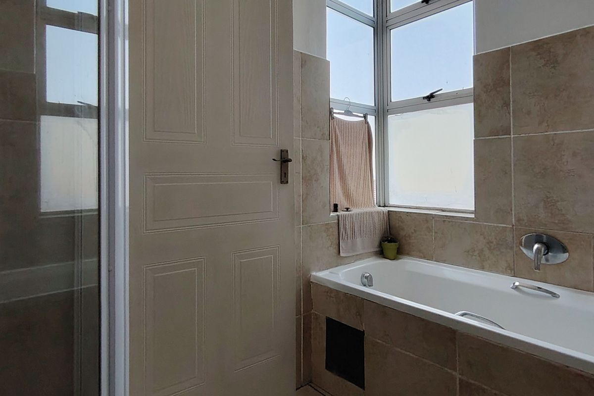 A functional bathroom featuring a bathtub, a separate shower enclosure, and neutral wall tiling with a window for natural light.