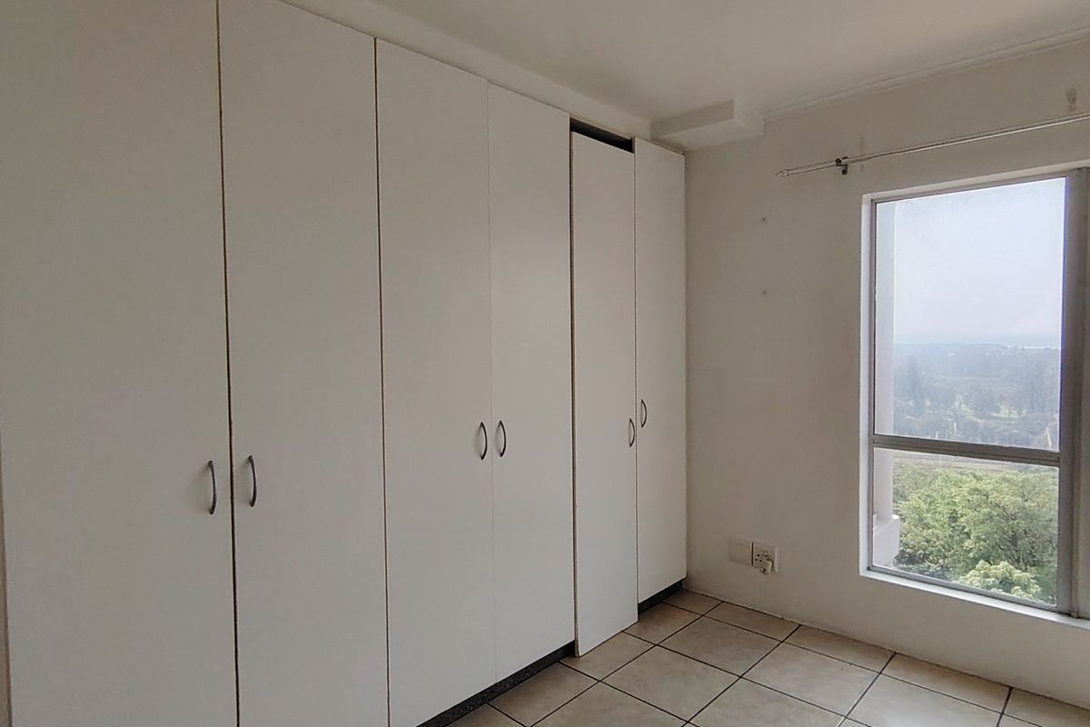 A bright, empty bedroom featuring white built-in cupboards, tiled flooring, and a large window offering an elevated view.