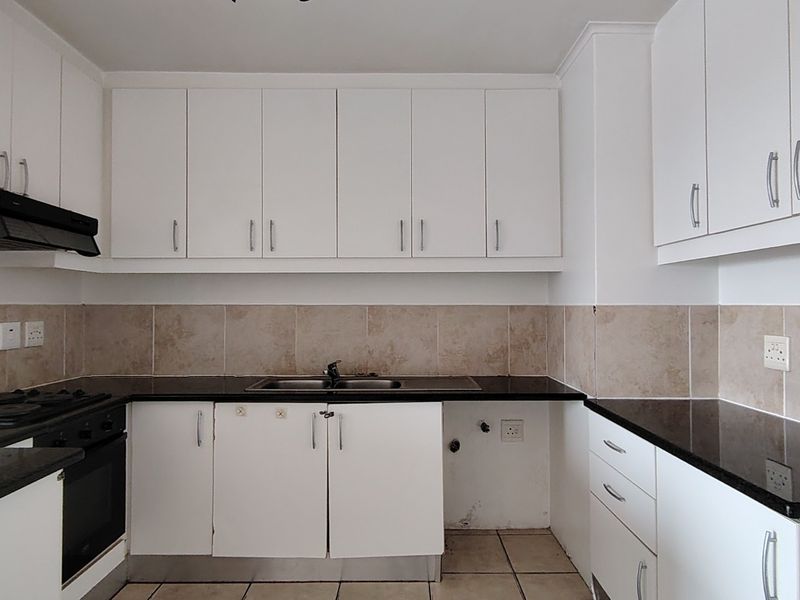 A functional kitchen featuring white cabinetry, dark granite countertops, a built-in oven, hob, and extractor fan with a neutral tiled backsplash.