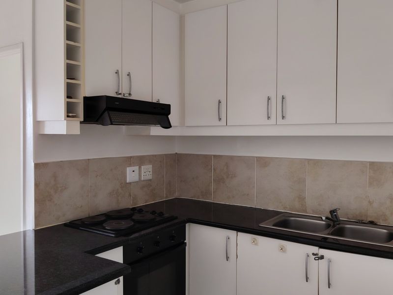 A clean, functional kitchen featuring white cabinetry, black granite countertops, a built-in oven, electric hob, and a stainless steel double sink.