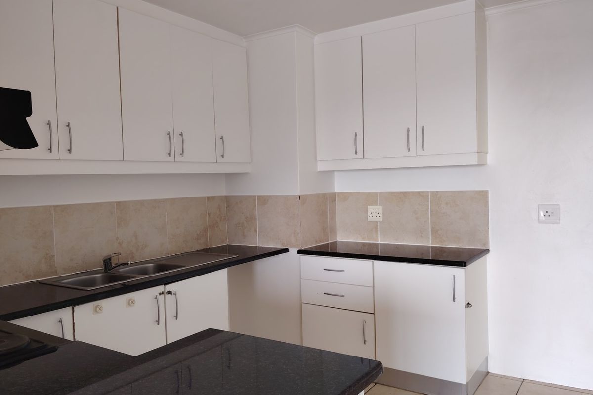 A clean, modern kitchen featuring white cabinetry, contrasting black granite countertops, a stainless steel double sink, and a neutral ceramic tile backsplash.