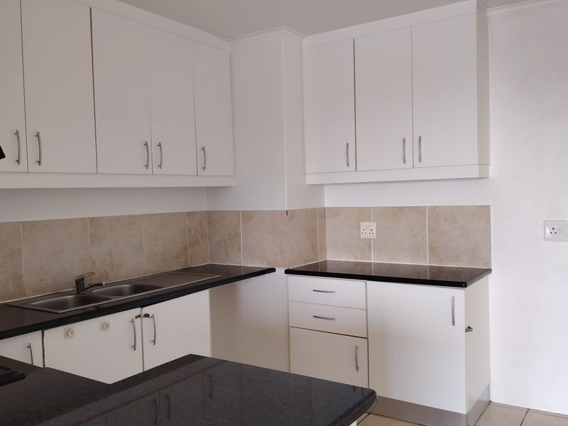 A clean, modern kitchen featuring white cabinetry, contrasting black granite countertops, a stainless steel double sink, and a neutral ceramic tile backsplash.
