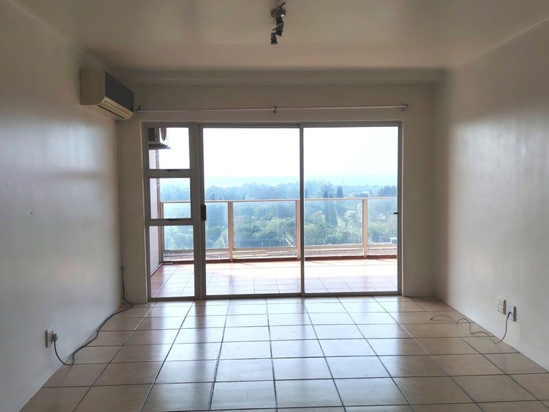An empty living room featuring tiled flooring, an air conditioning unit, and large sliding glass doors leading to a balcony with scenic views.