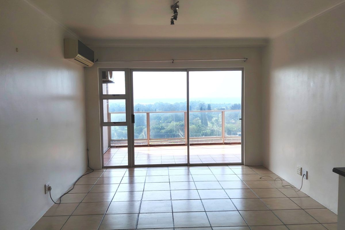 An empty living room featuring tiled flooring, an air conditioning unit, and large sliding glass doors leading to a balcony with scenic views.