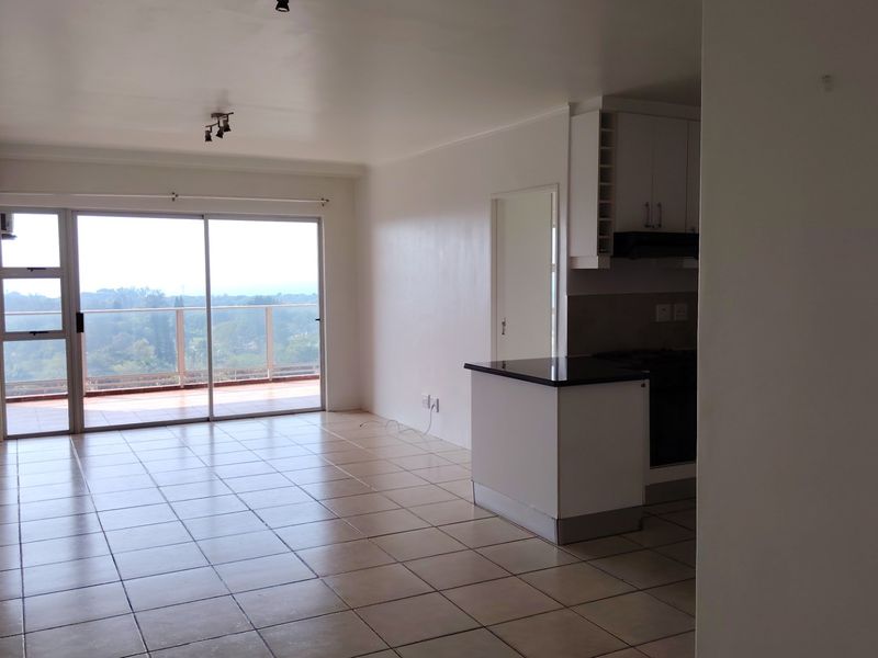 Spacious open-plan living area featuring tiled floors, a modern kitchen island, and large sliding doors leading to a balcony with scenic views.