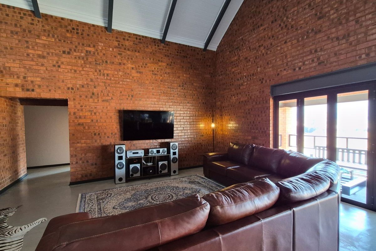 Spacious living room featuring high vaulted ceilings with exposed beams, striking face-brick walls, polished concrete floors, and large sliding doors leading to the patio.