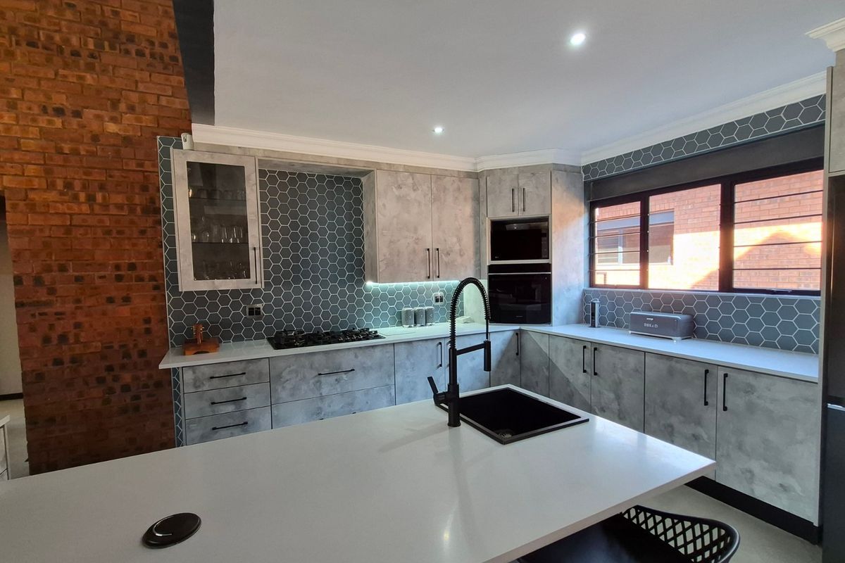 Modern kitchen featuring concrete-look cabinetry, stone countertops, a central island with a black sink, gas hob, and a striking exposed brick feature wall.
