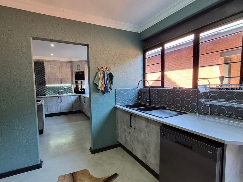 A functional scullery featuring modern grey cabinetry, hexagonal tile backsplash, double sink, and integrated dishwasher, with a seamless transition to the main kitchen area.