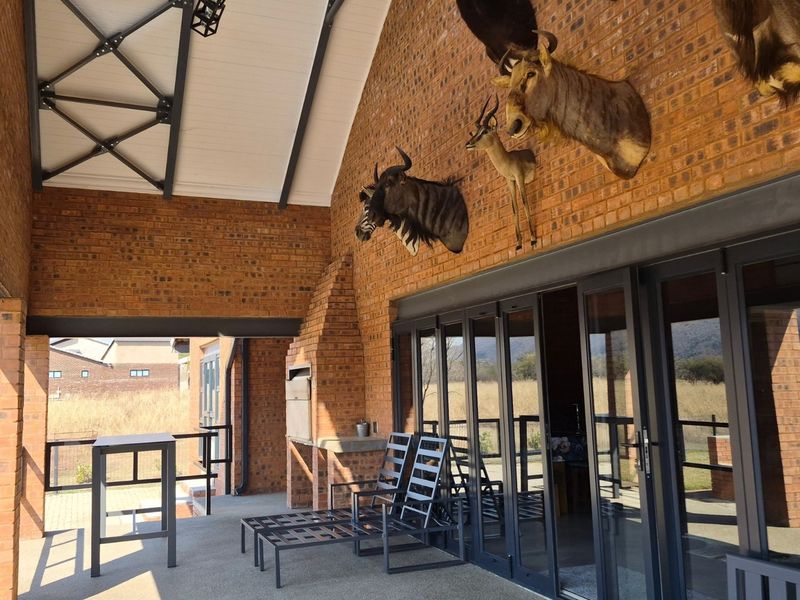 Spacious covered patio featuring exposed brickwork, steel roof trusses, a built-in braai, and large folding glass doors leading to the interior.