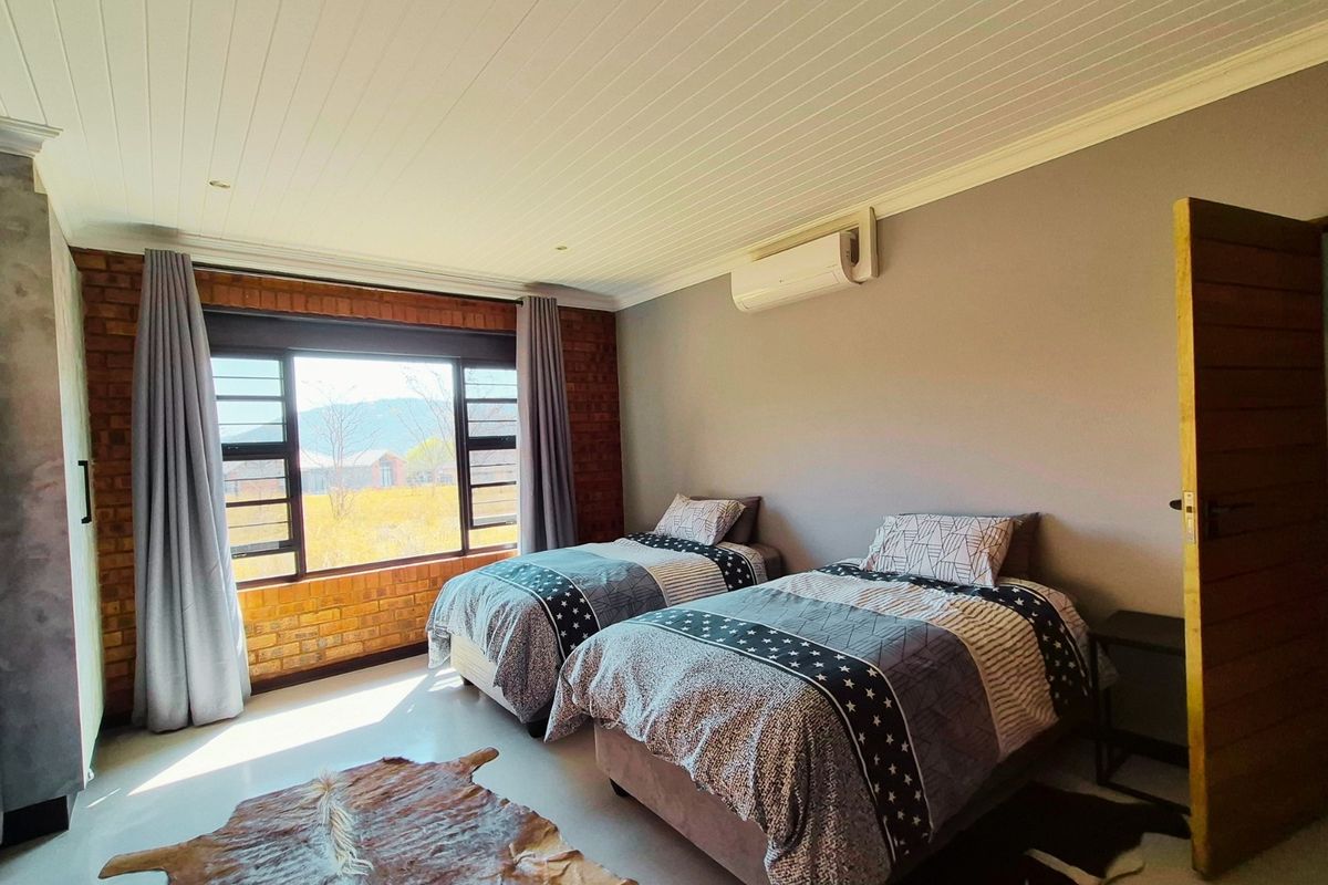 A well-maintained bedroom featuring an exposed brick feature wall, timber ceiling, and wall-mounted air conditioning unit with views of the surrounding landscape.