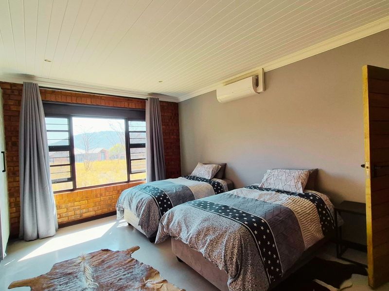 A well-maintained bedroom featuring an exposed brick feature wall, timber ceiling, and wall-mounted air conditioning unit with views of the surrounding landscape.