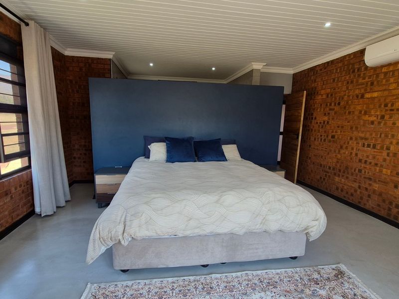 Spacious bedroom featuring exposed brick walls, polished concrete flooring, a tongue and groove ceiling, and a wall-mounted split system air conditioner.