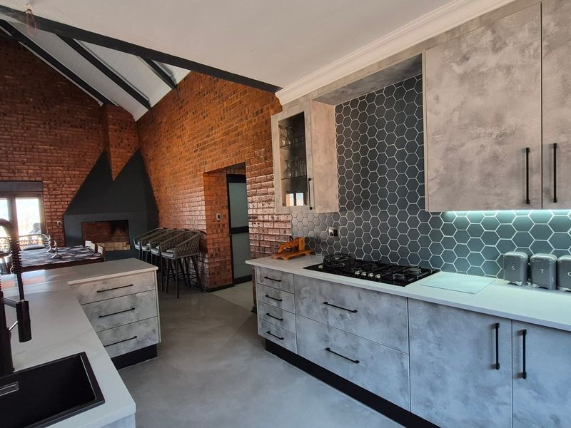 Modern open-plan kitchen featuring concrete-look cabinetry, hexagonal tile backsplash, and a large island, seamlessly integrated with a spacious living area with exposed brick walls.