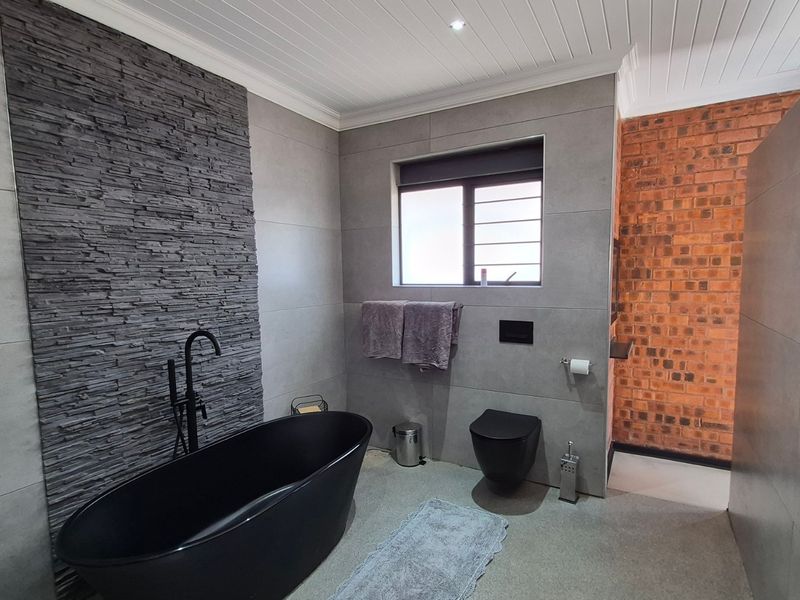 Modern bathroom featuring a sleek black freestanding bathtub, wall-mounted toilet, striking slate feature wall, and exposed brick accents with contemporary finishes.