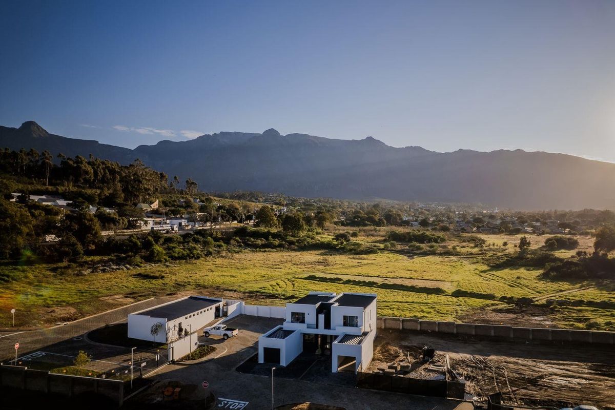 Aerial view of a modern townhouse development featuring flat roofs, paved driveways, and perimeter walls, set against a scenic mountain landscape.