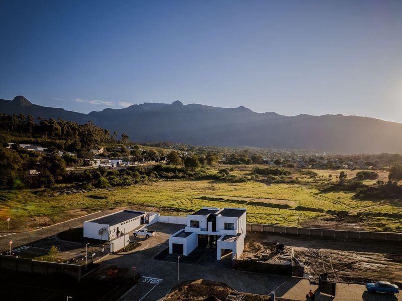 Aerial view of a modern townhouse development featuring flat roofs, paved driveways, and perimeter walls, set against a scenic mountain landscape.