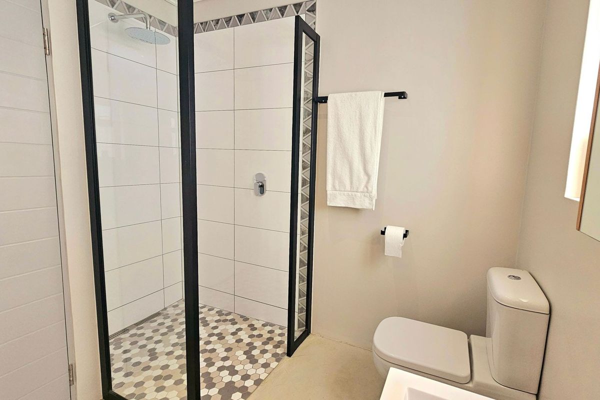 Modern bathroom featuring a walk-in shower with black frame, rainfall shower head, hexagonal floor tiling, and contemporary wall-mounted toilet.