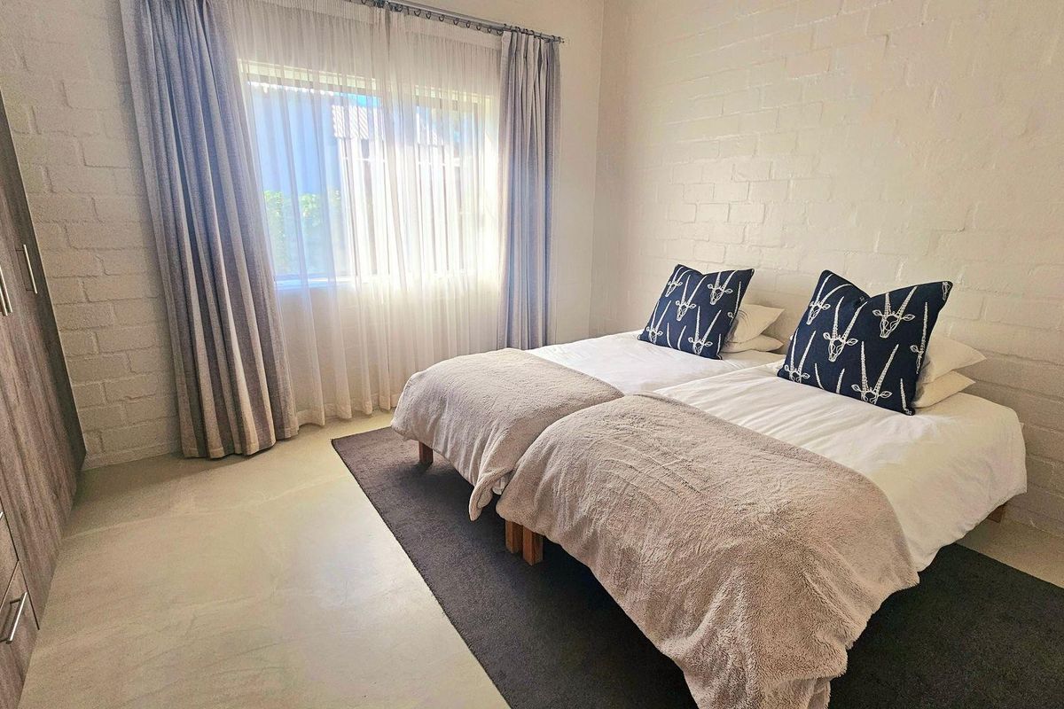 A well-maintained bedroom featuring a painted brick feature wall, neutral flooring, and a built-in wardrobe.
