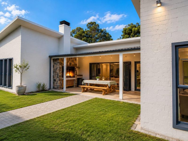 Covered patio area featuring a built-in stone-clad braai, tiled flooring, and seamless access to the interior through bi-fold doors, overlooking a landscaped garden.