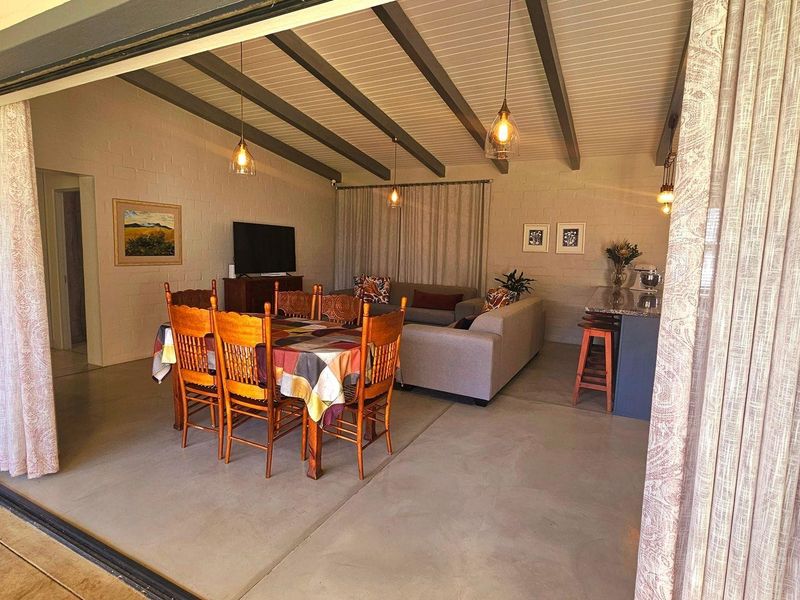 Spacious open-plan living and dining area featuring exposed ceiling beams, polished concrete floors, and large sliding doors opening to the outdoors.