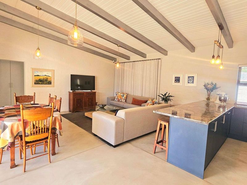 Spacious open-plan living area featuring exposed ceiling beams, a modern kitchen island with granite countertops, and integrated cabinetry.