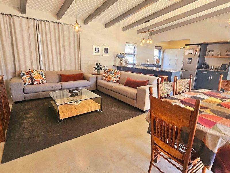 Spacious open-plan living and dining area featuring exposed ceiling beams, polished concrete floors, and a modern kitchen with a central island and granite countertops.