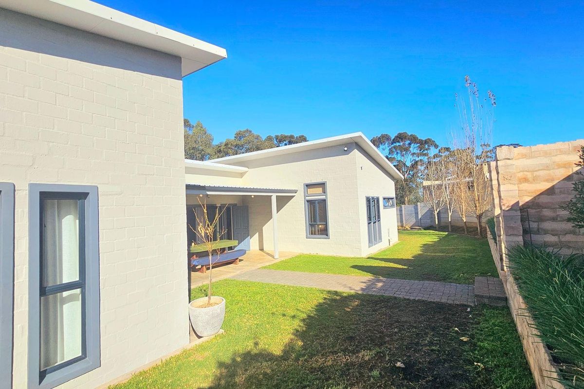 A well-maintained rear exterior view of the house featuring a covered patio, paved walkway, and a neat garden area with a retaining wall.