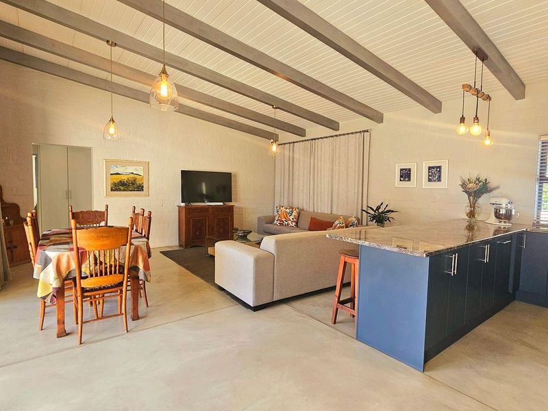 Spacious open-plan living area featuring exposed ceiling beams, polished concrete floors, and a modern kitchen island with granite countertops and direct patio access.