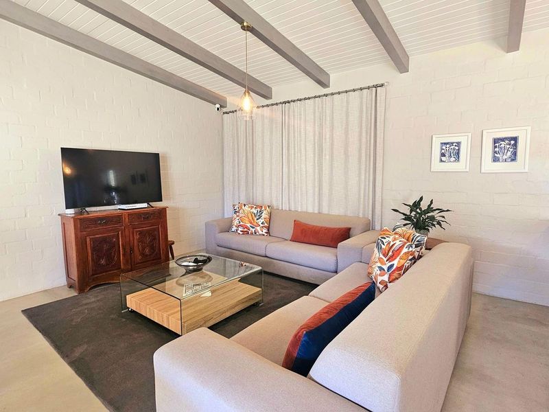 A bright living room featuring exposed ceiling beams, painted brick walls, and a breakfast bar, creating a comfortable and inviting open-plan living space.