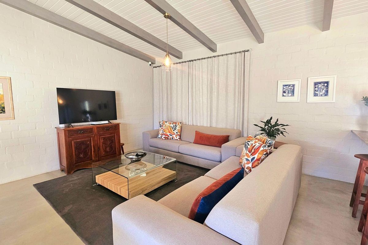 A bright living room featuring exposed ceiling beams, painted brick walls, and a breakfast bar, creating a comfortable and inviting open-plan living space.