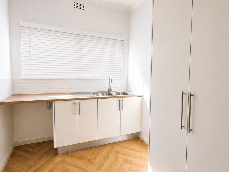 A clean and modern laundry room featuring white cabinetry, a wooden countertop, stainless steel sink, and stylish herringbone flooring.